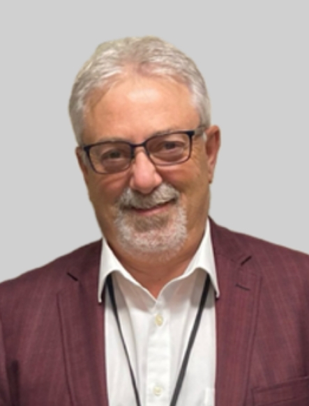Portrait de Richard Côté, souriant, portant un veston bordeaux.