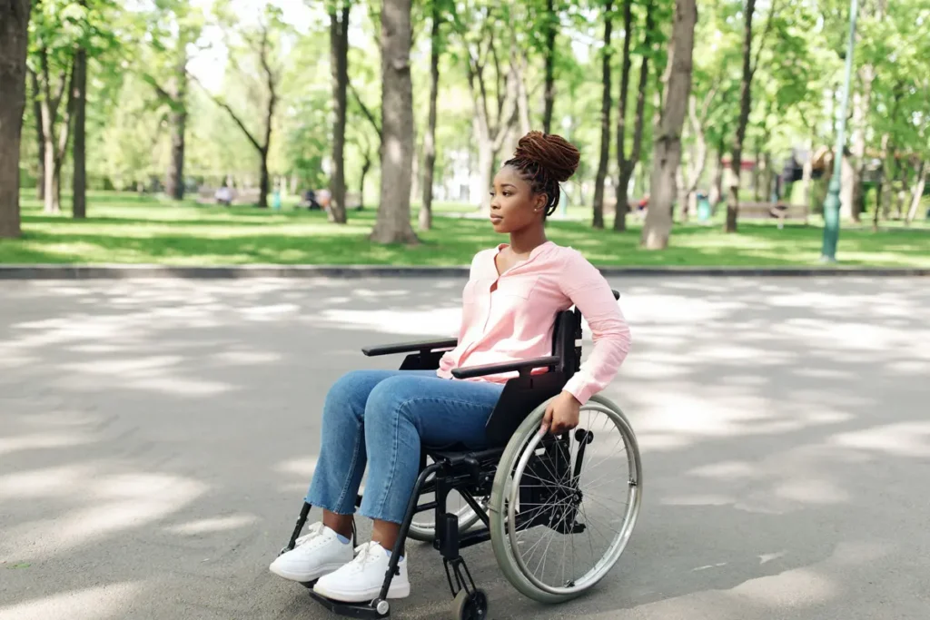 Jeune femme en fauteuil roulant dans un parc, portant un chandail rose.