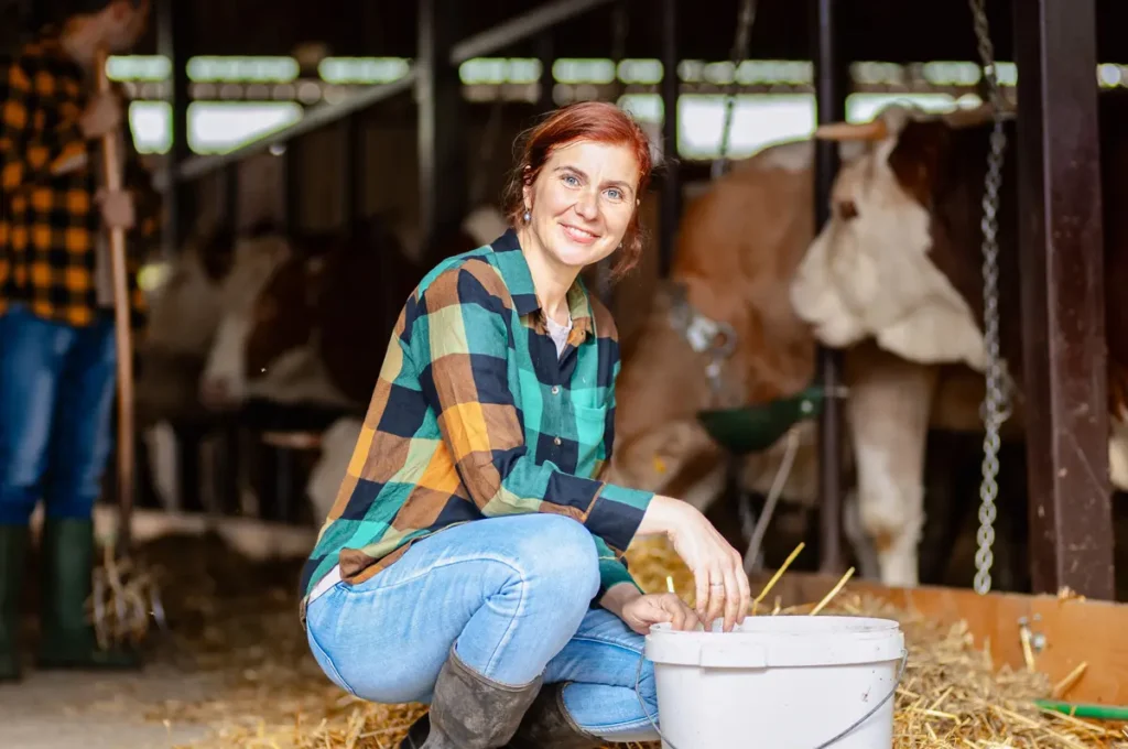 Femme agricultrice souriante agenouillée dans une étable, près d'une vache.